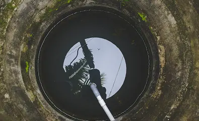 Top-down view inside a concrete well with a water pump pipe visible at the bottom