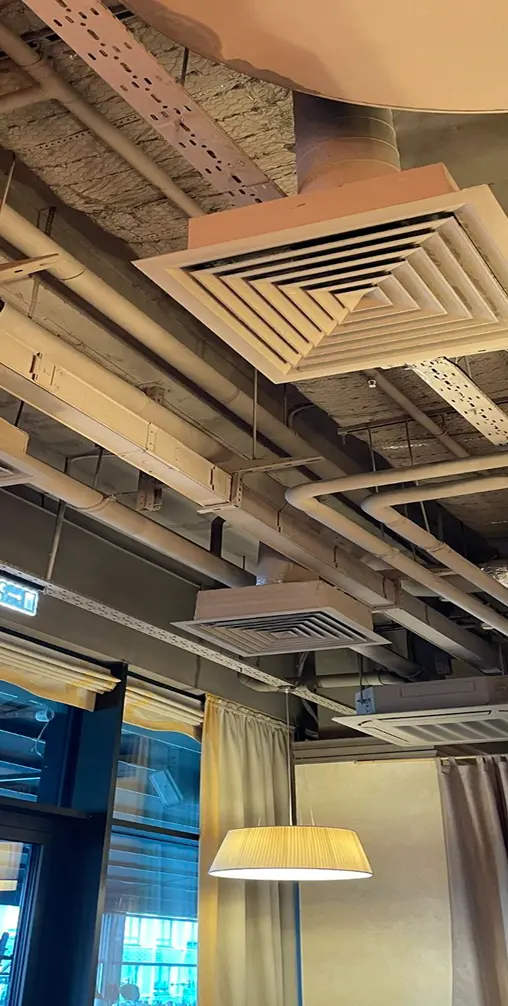 Ceiling-mounted cassette air conditioning units with exposed ductwork and pipes in a commercial interior space