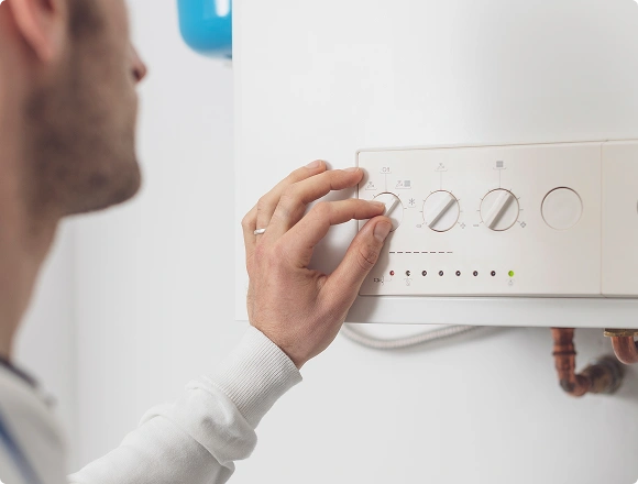 Technician adjusting the control panel dials on a wall-mounted boiler unit