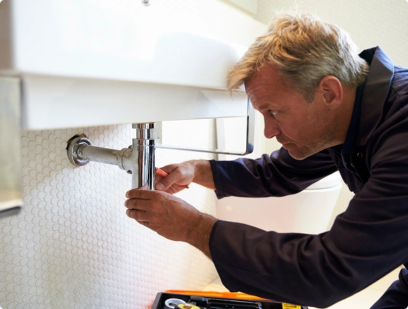 Plumber repairing the chrome P-trap drain pipe under a wall-mounted bathroom sink