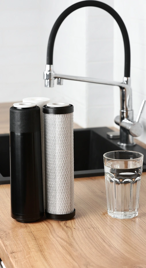 Water filtration system with replacement cartridges and a glass of water on a kitchen countertop