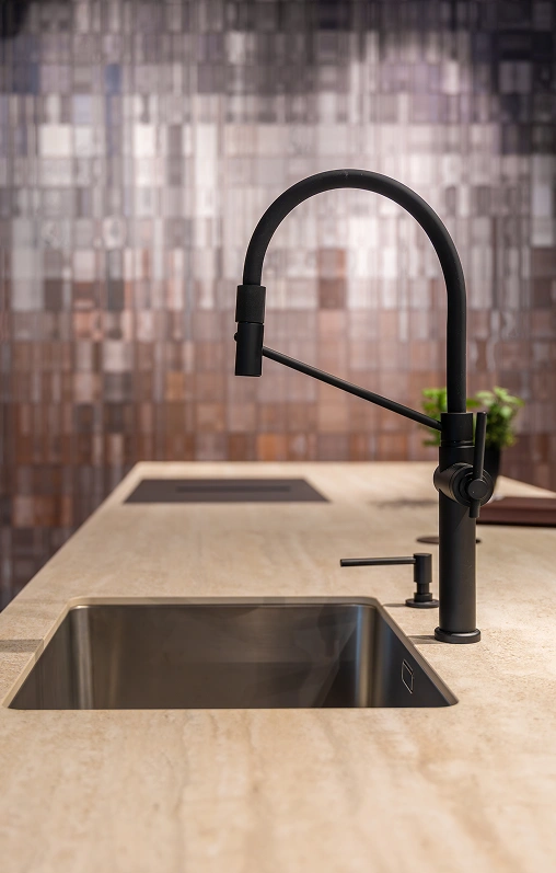 Black pull-down kitchen faucet and undermount stainless steel sink set in a beige travertine countertop against a glossy mosaic tile backsplash