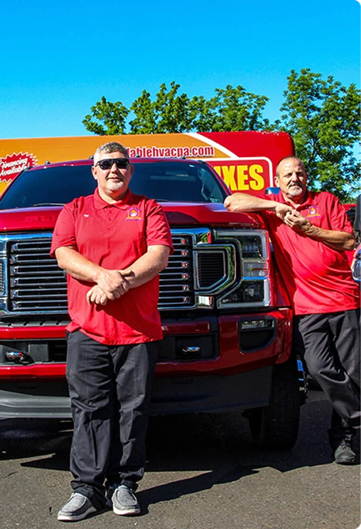Two men in red polo shirts leaning on a red company pickup truck on a sunny day.